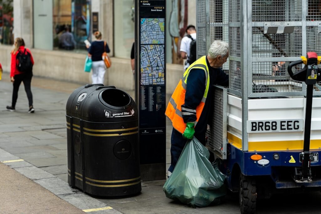 a-man-standing-next-to-a-trash-can-on-the-side-of-a-road-14mpvqbdj0m